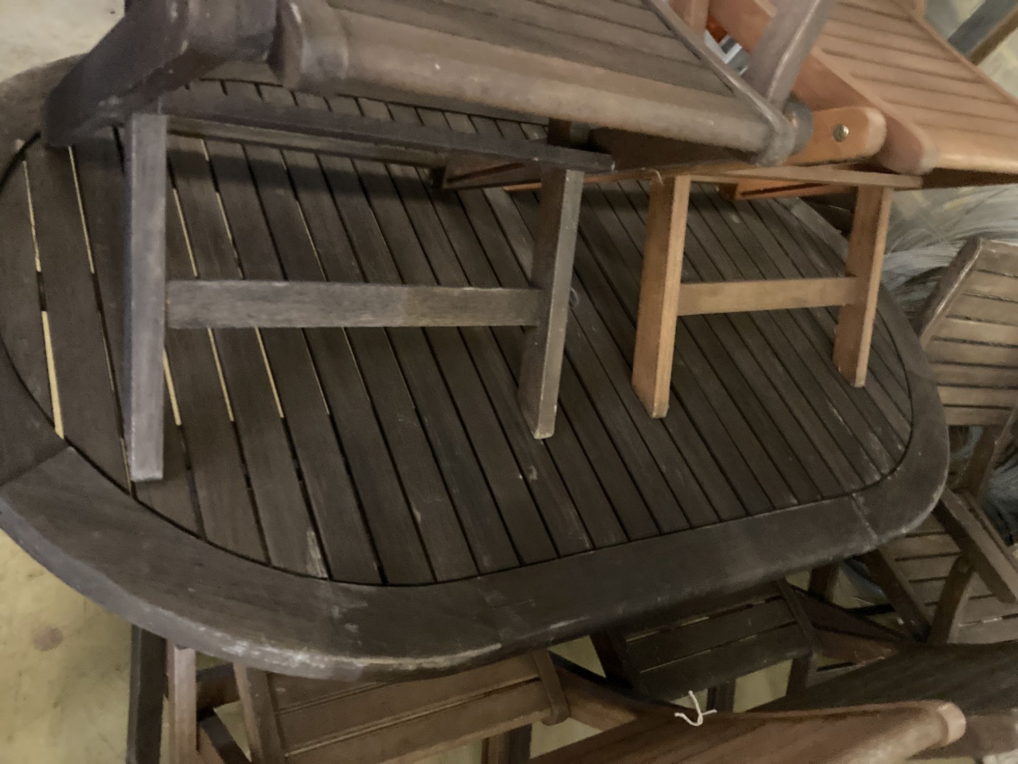 A weathered teak garden table and six teak folding chairs (two with arms)